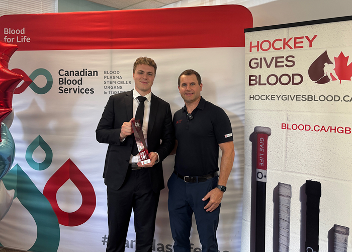 Carson Wetsch with Stu standing in front of Canadian Blood Services and Hockey Gives Blood banner stands
