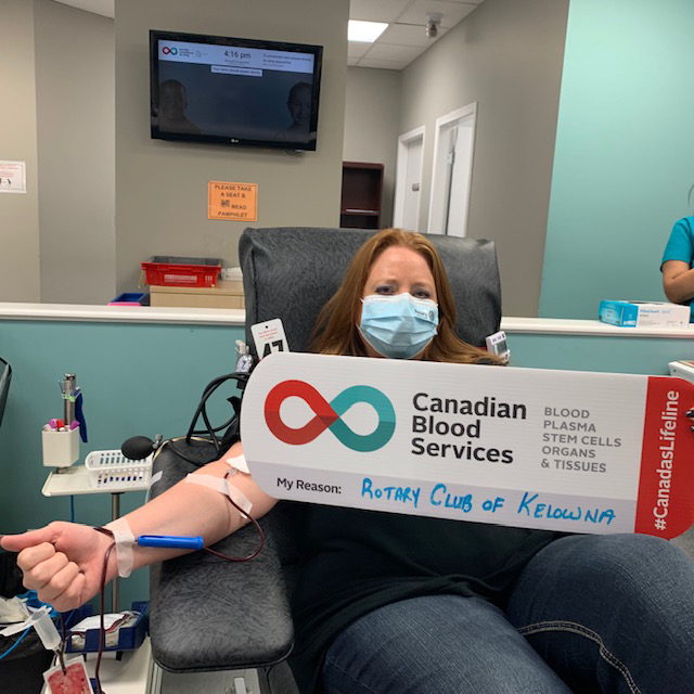Image of Lenetta Parry sitting in the chair donating blood holding up a My Reasons sign at the donor centre