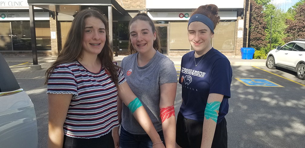 Triplet sisters showing bandaged arms after first blood donation