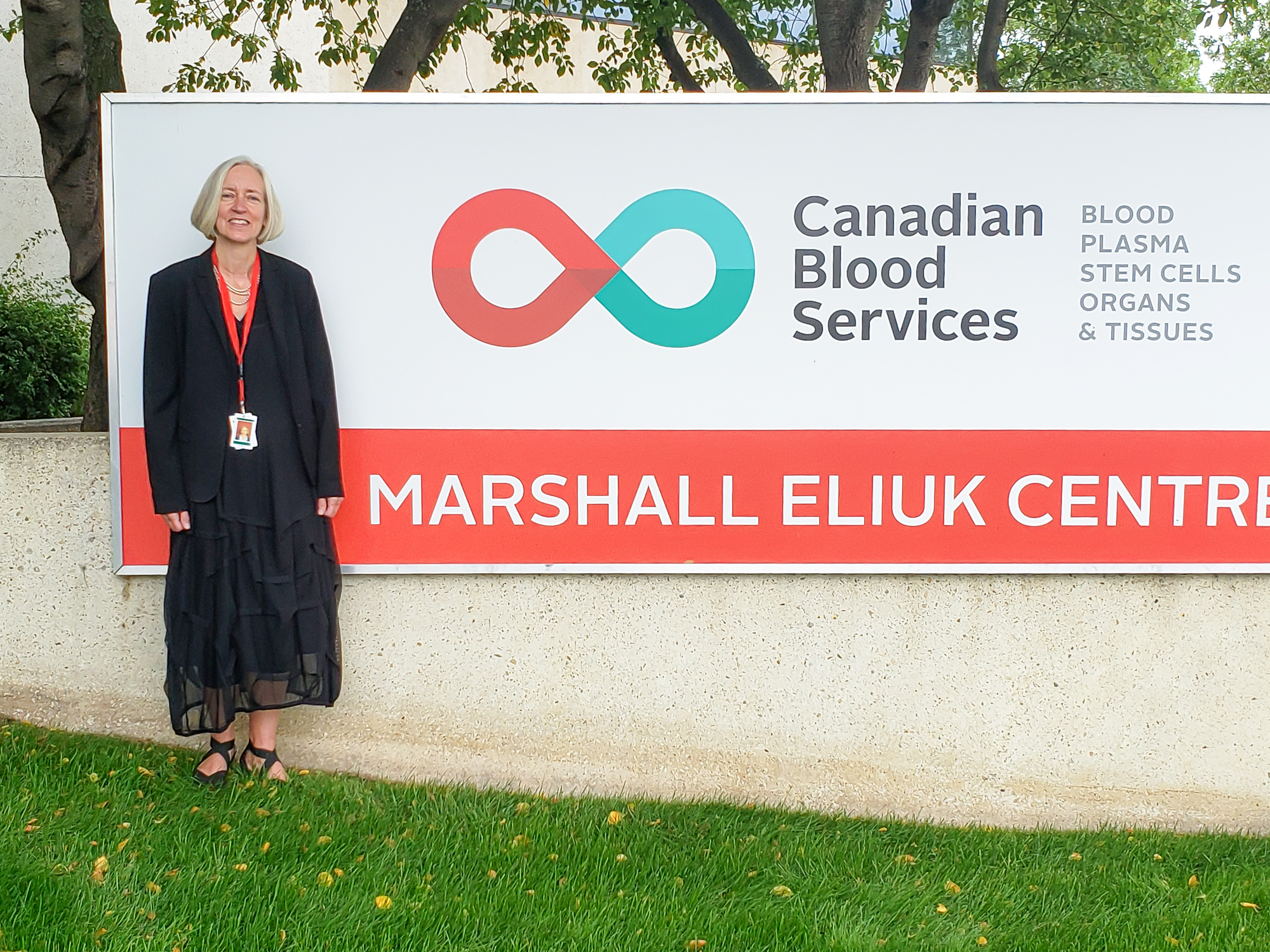 Image of Dr. Gwen Clarke standing out of the Canadian Blood Services building sign at Marshall Eliuk Centre