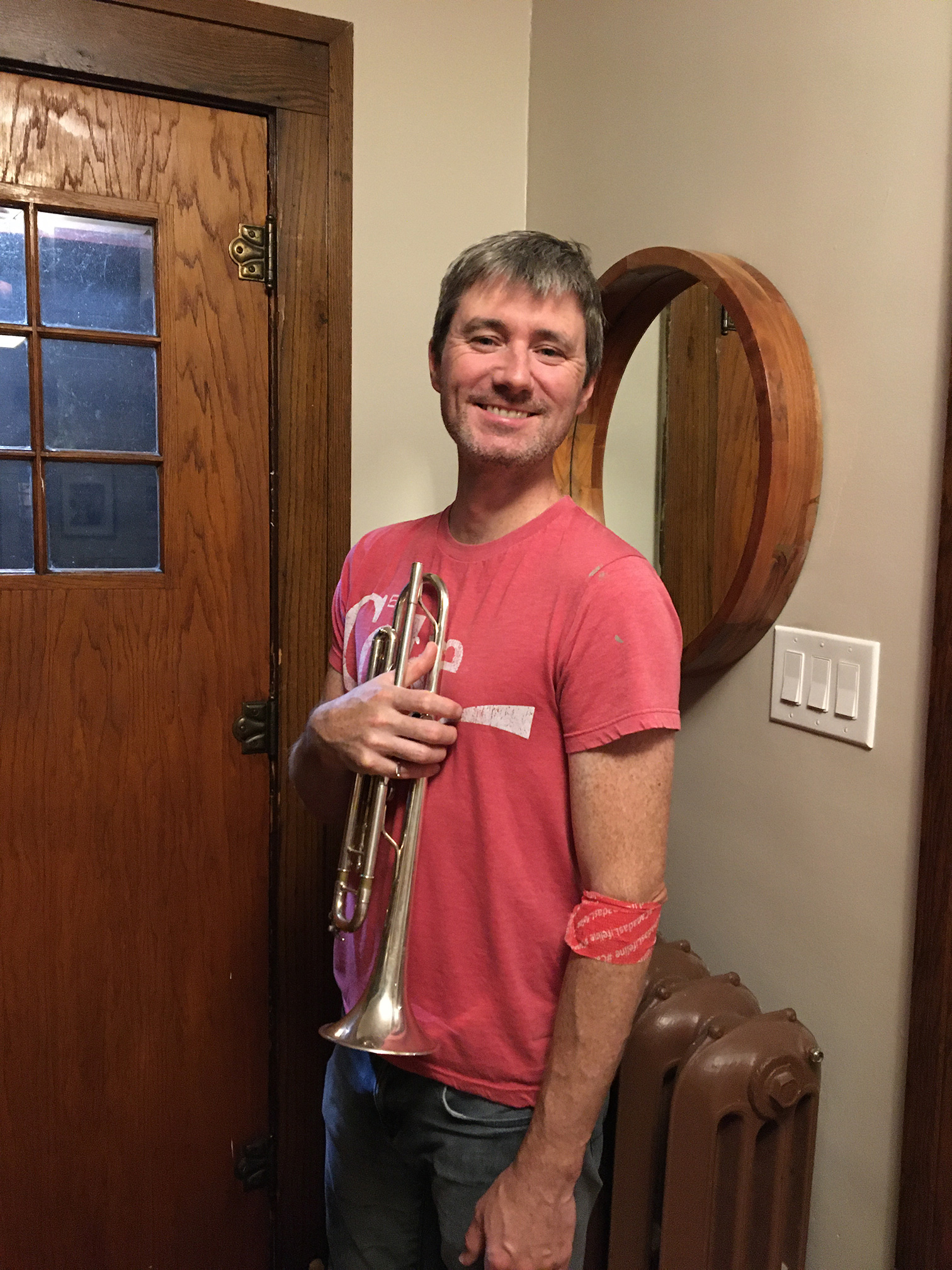 Image of blood donor Isaac Pulford holding a trumpet wearing a red shirt standing near the front door.