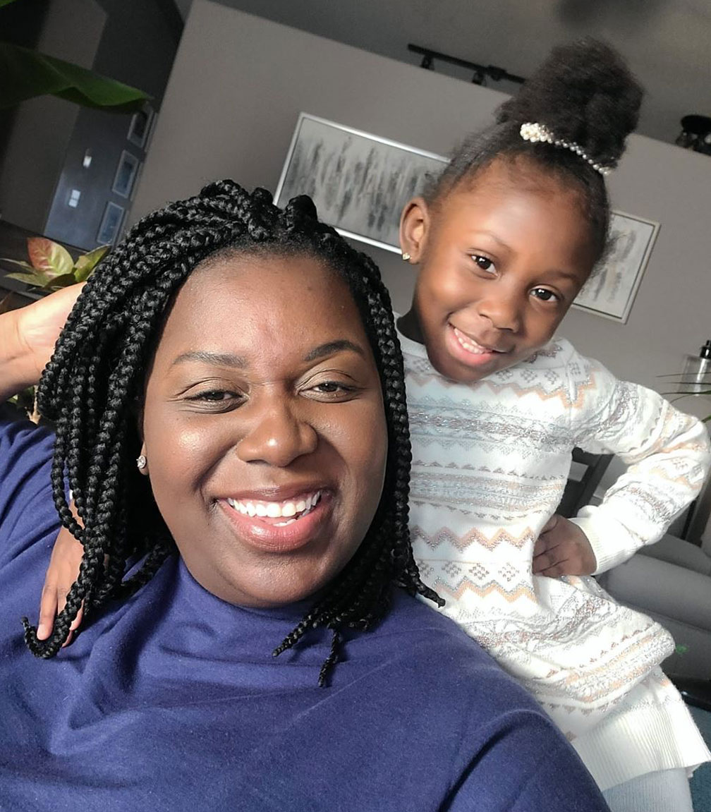 Mother with preschool daughter behind her, hand on hip