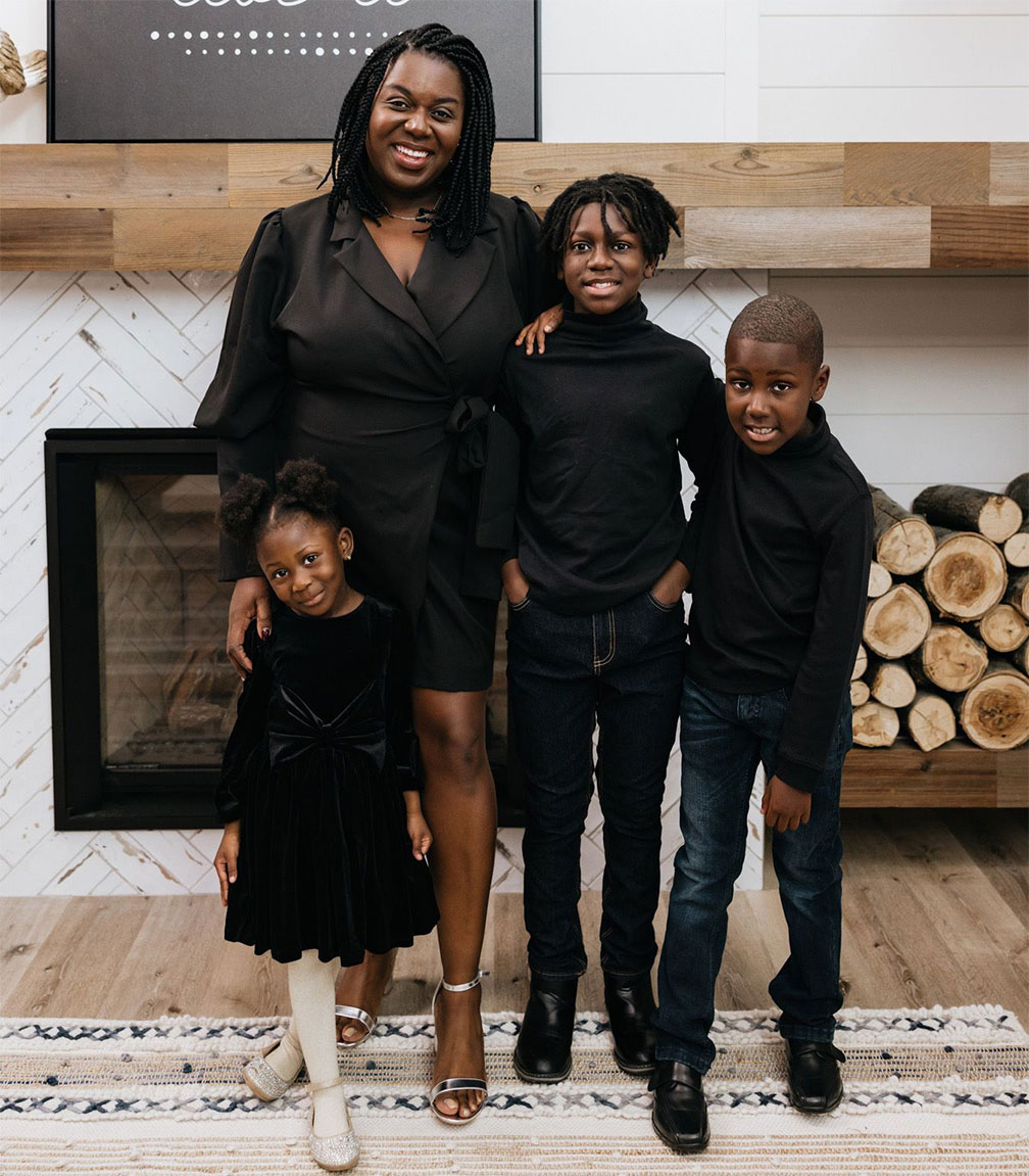 Mother, preschool age daughter and two school age sons in front of fireplace and firewood