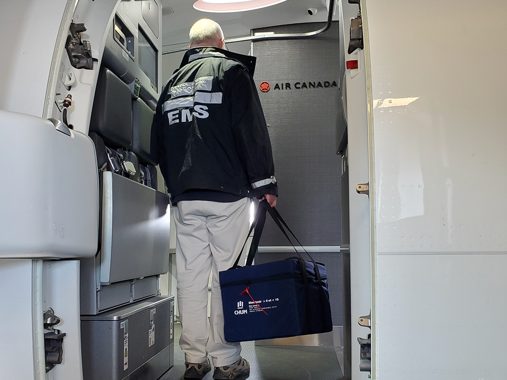 A man in a black jacket carrying a blue cooler containing a donated kidney stands in the entrance of an Air Canada plane.