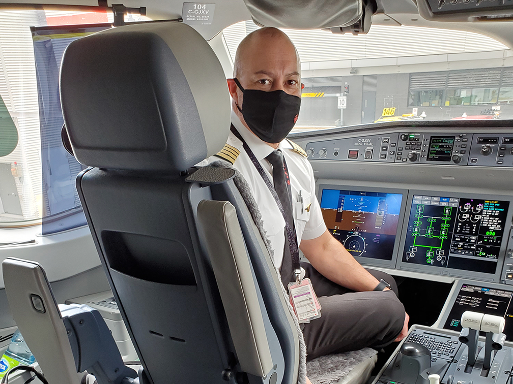 Air Canada pilot sits in his chair in the flight deck of a plane. A blue cooler containing a donated kidney is placed behind his chair.