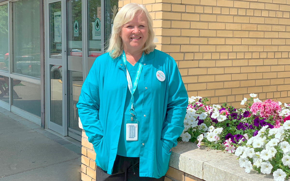 A woman in a blue scrubs stands outside a building.