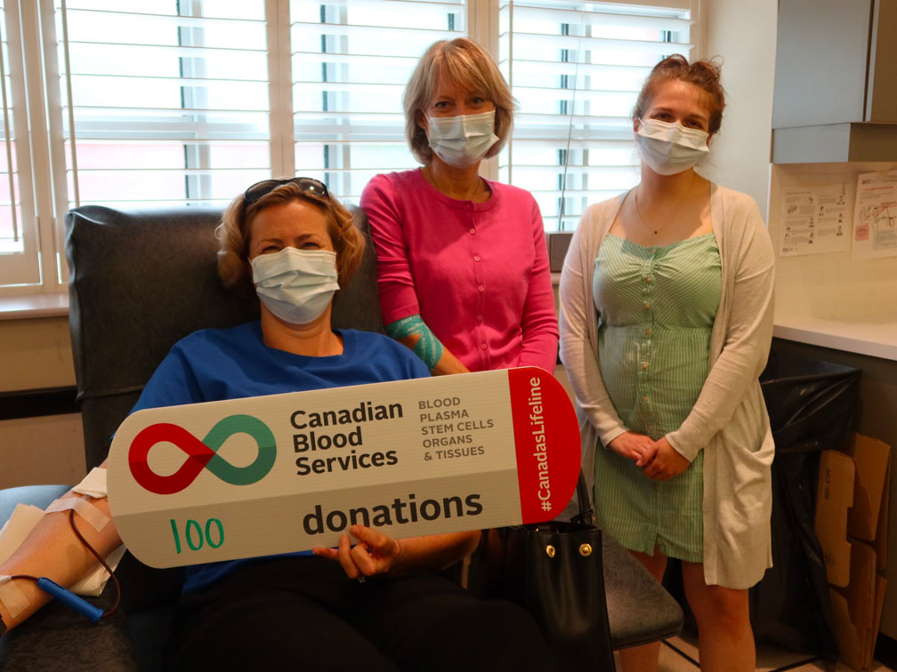 A blood donor makes her 100th donation with Canadian Blood Services employees nearby