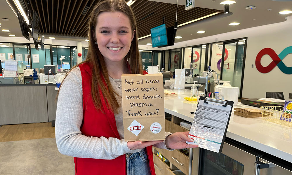 young woman standing by donor centre counter holding small signs