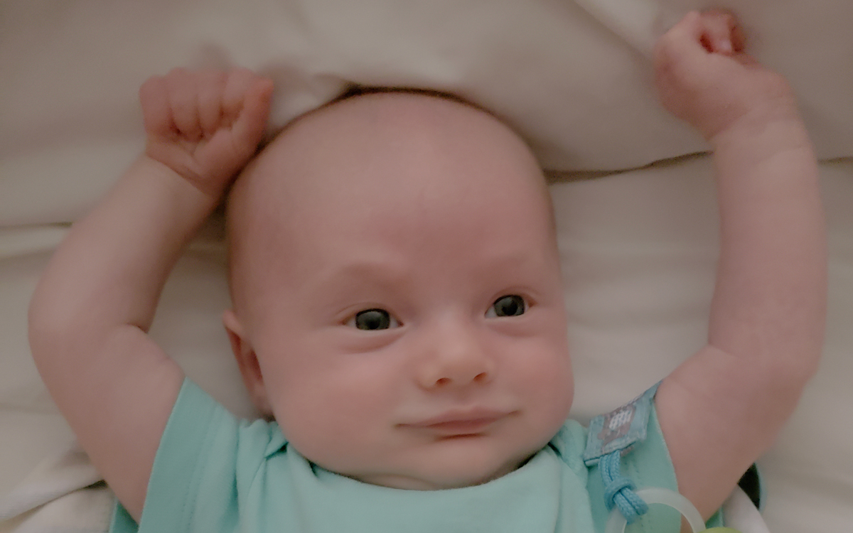 six-month-old baby in a green jumper lying in crib with arms stretched overhead