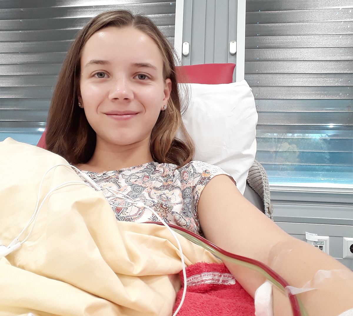 A smiling young woman lies in a hospital bed donating stem cells for transplant.
