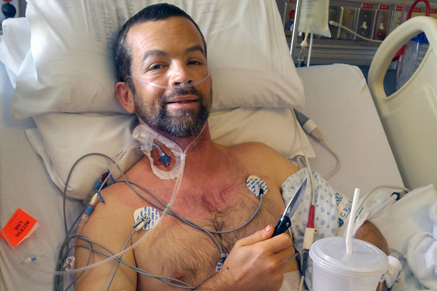 Man in hospital bed with many tubes in his body, holding knife