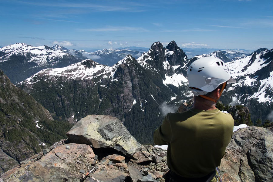 Man in helmet on mountain looking out at other peaks