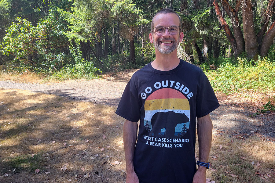 Man wearing a black T-shirt that says “Go outside. Worst case scenario a bear kills you.”