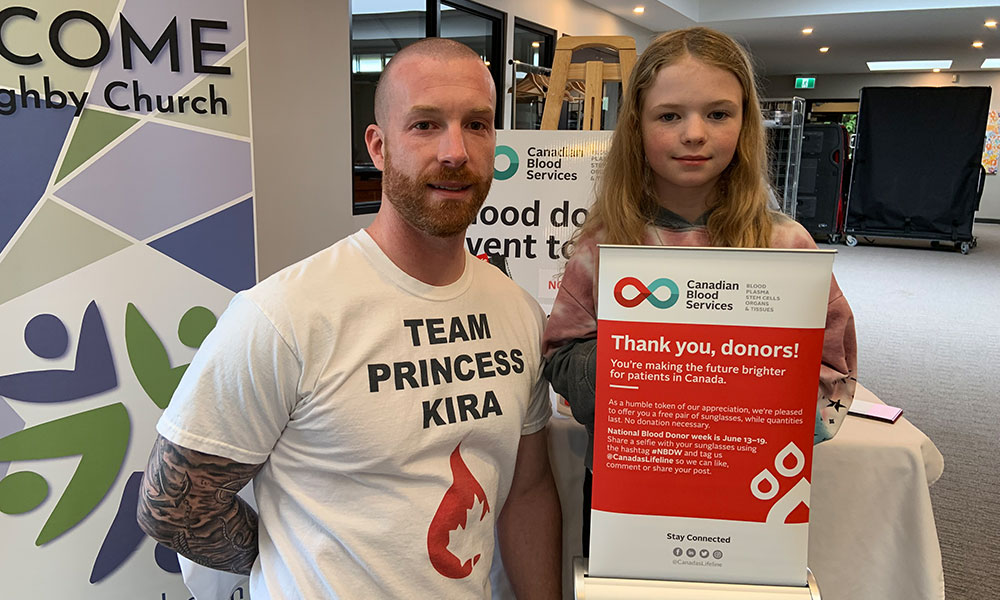 Adult male standing next to a young girl holding a sign