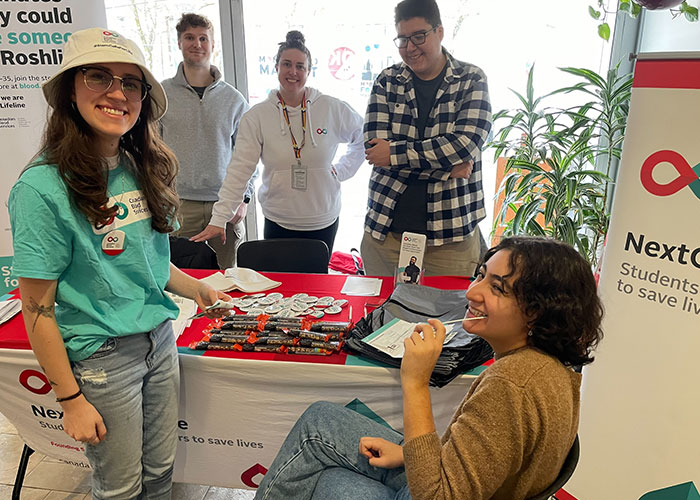 Stem cell club volunteers with someone with has a swab in their mouth sitting down at a booth.