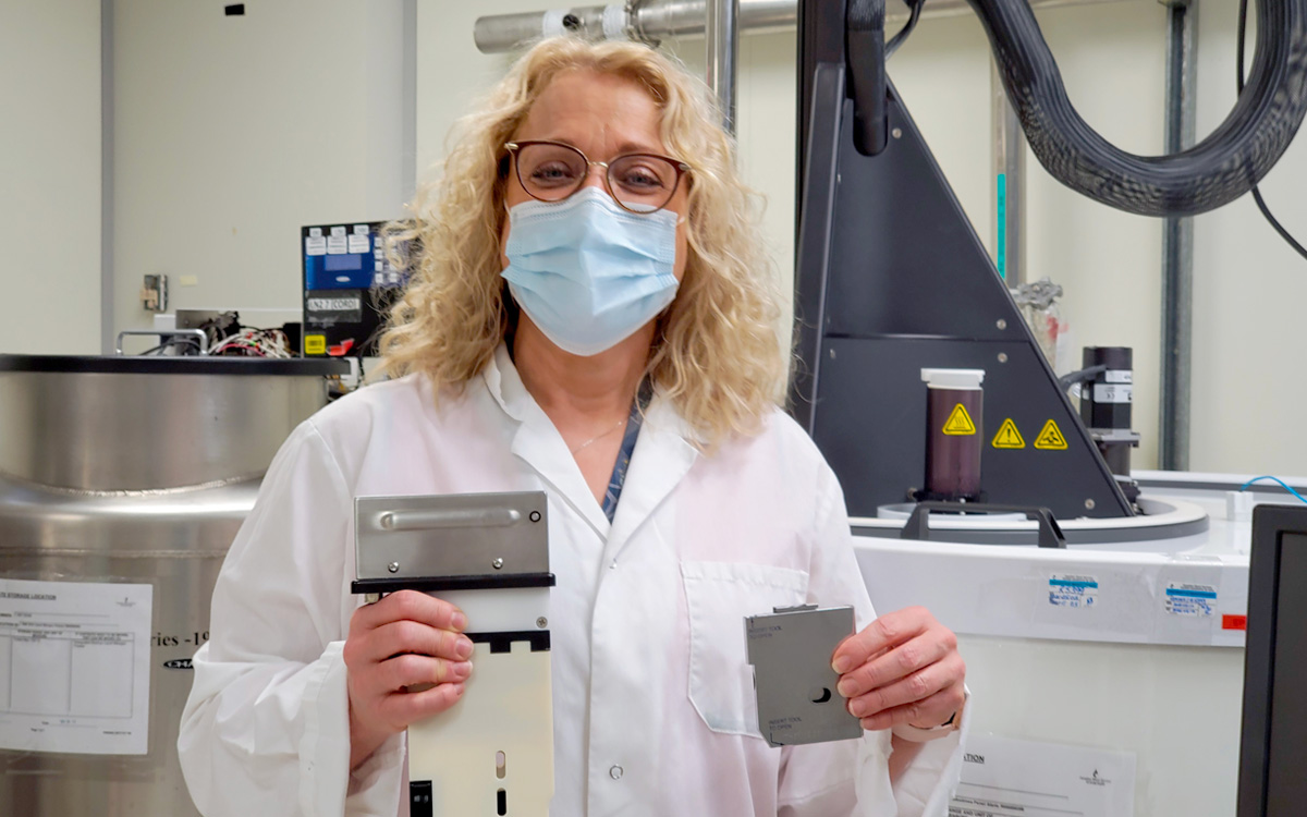 A long blonde medical laboratory technologist holds a cassette used to store frozen cord blood and a control rate freezer.