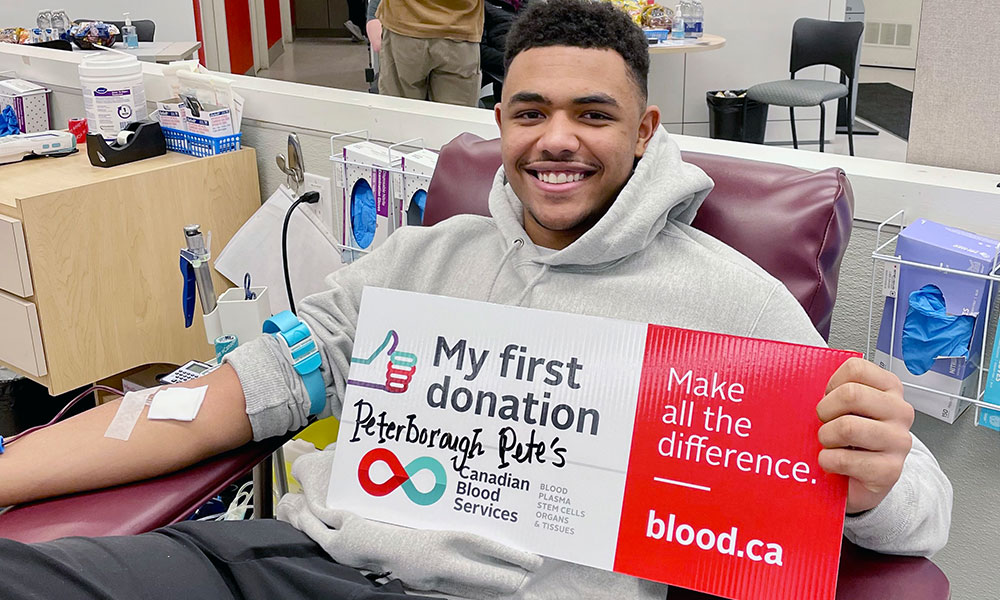 Blood donor in donation chair with a sign that says “My first donation.”