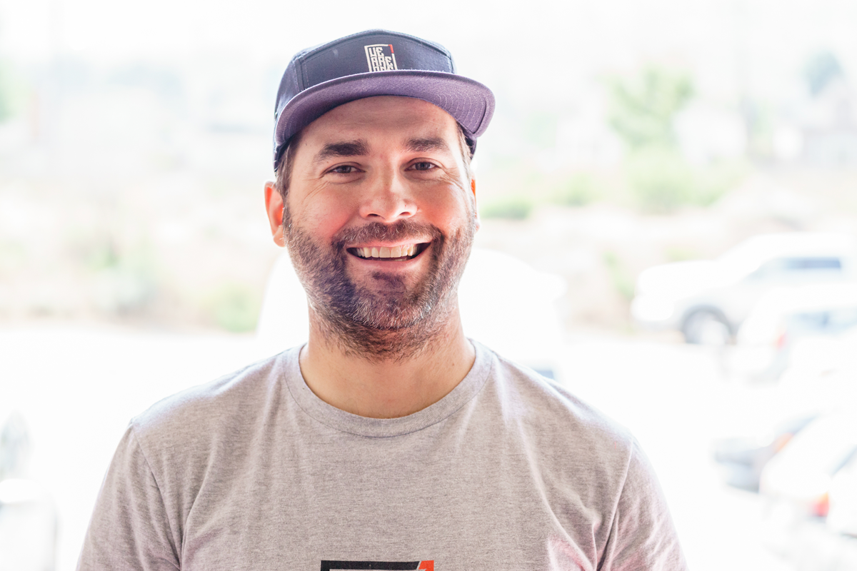 Dustin Adams, owner of We Are One Composites in Kamloops, B.C. standing outside with cars in the background wearing a baseball cap.