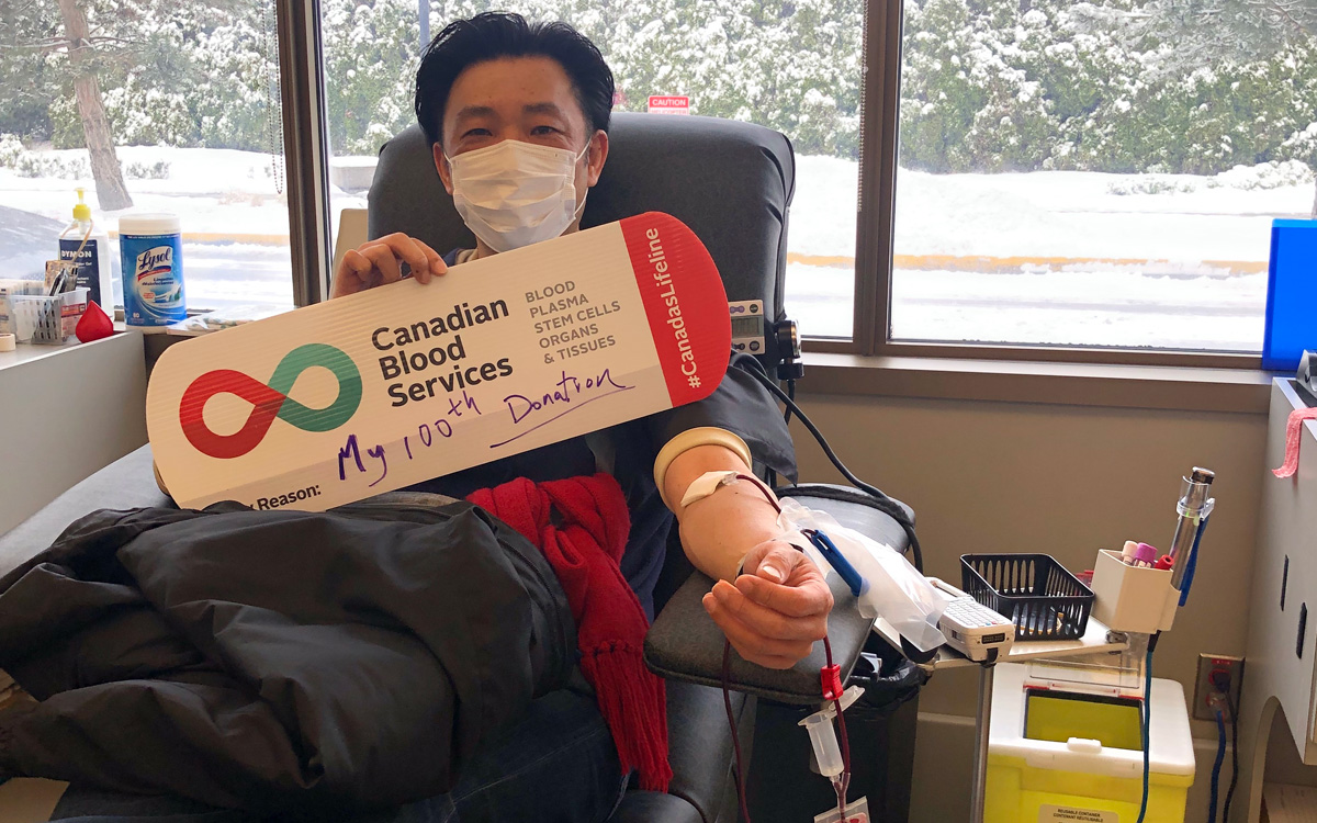 Man donates blood with Canadian Blood Services sign on his lap