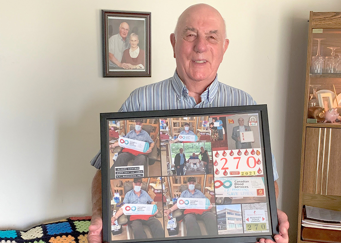 An 87-year-old man in a striped shirt holds a frame filled with mementoes of his blood donations.