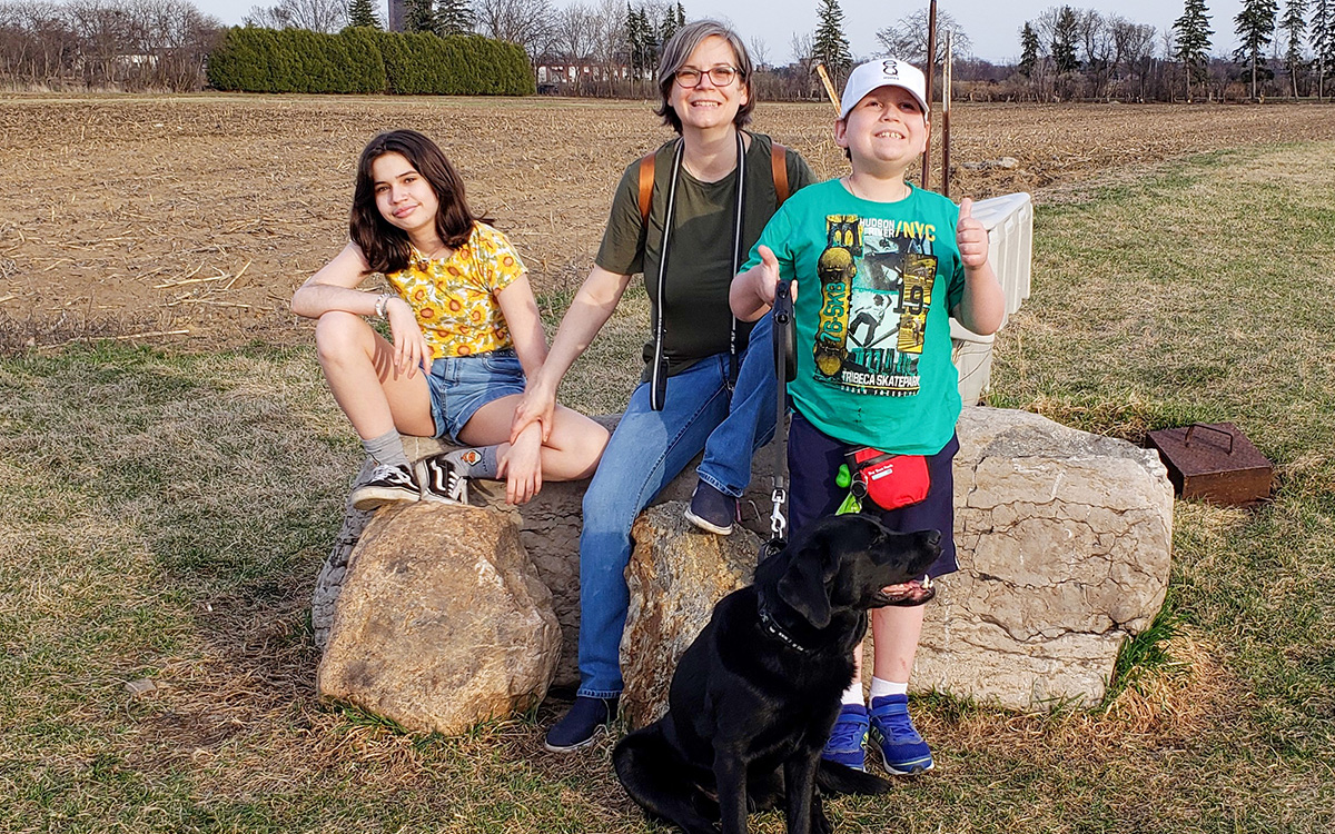 A mother, daughter, son and dog sit on some rocks during a family walk.