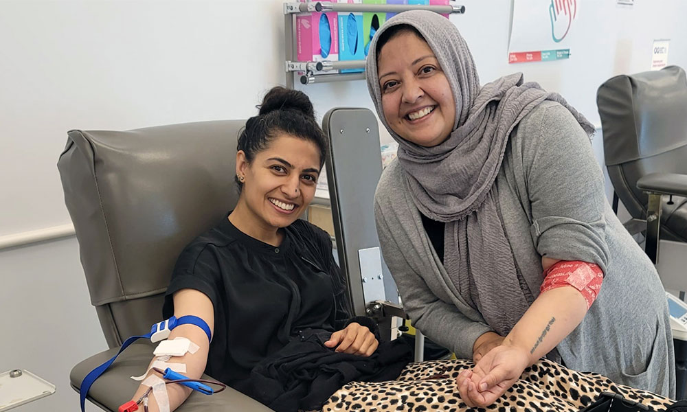 Woman donating blood with another blood donor with bandaged arm next to her