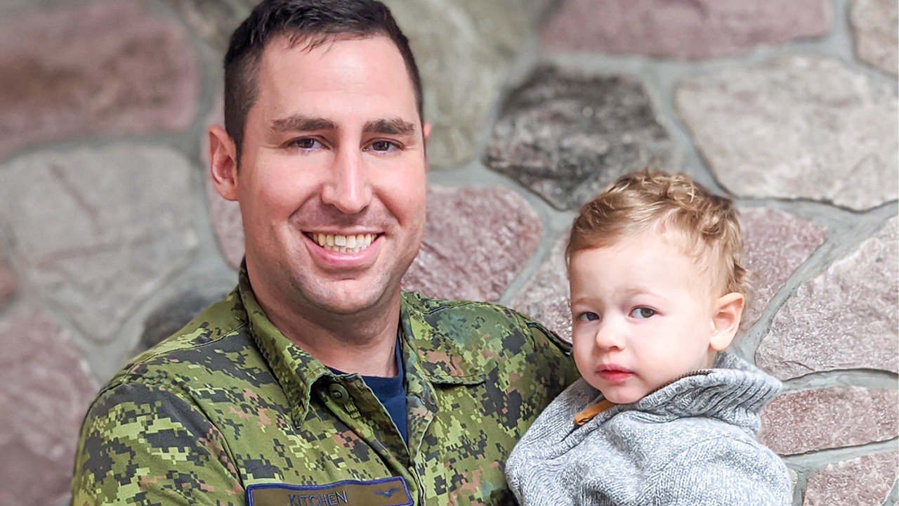Image of blood donor and registered organ donor Greg Kitchen holding son Cole Kitchen standing in front of a stone wall
