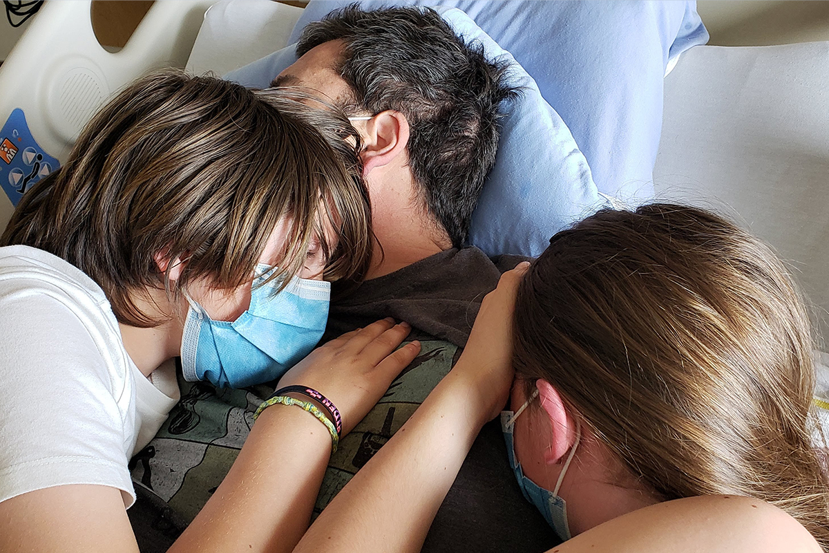 Stem cell recipient Greg Duerksen cuddles his children on his hospital bed.