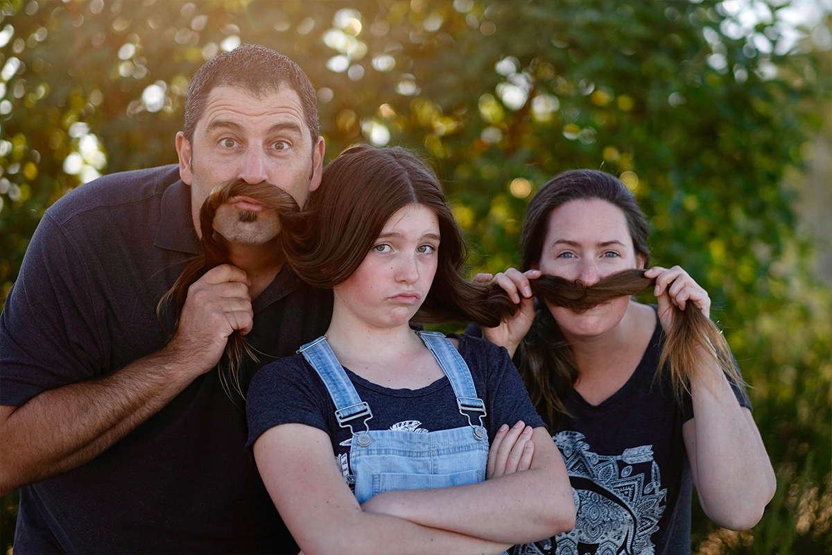 Stem cell recipient Greg Duerksen and his wife hold their daughter’s hair against their upper lips to make pretend moustaches.