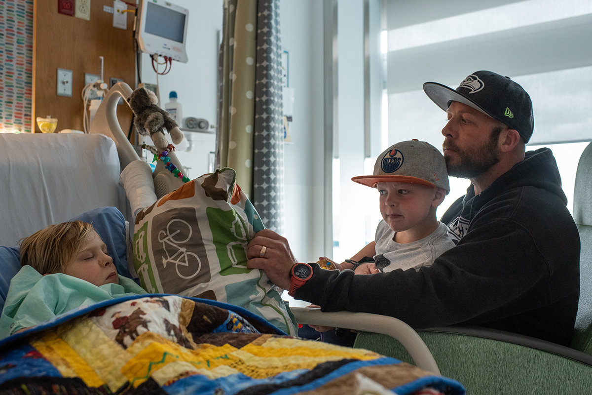 Harrison Wolfe holds his son Maverick as they peek in at Kane Wolfe asleep in hospital bed