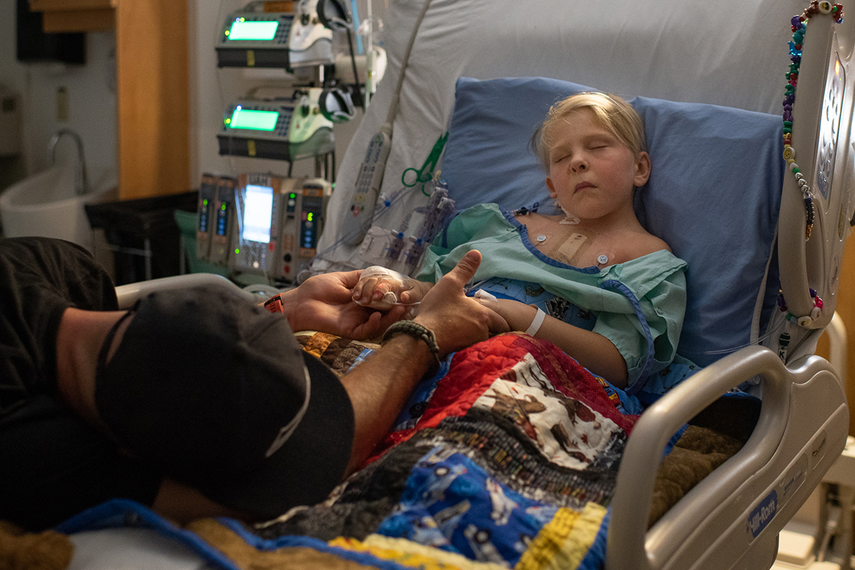 Harrison Wolfe holds his son’s hands while son sleeps in hospital room