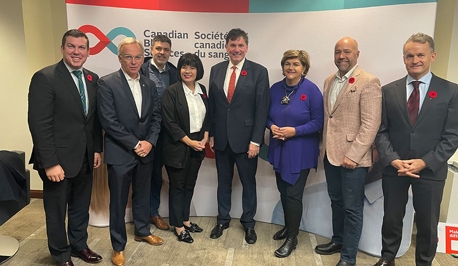 A group of Ministers and Members of Parliament pose in front of a Canadian Blood Services
