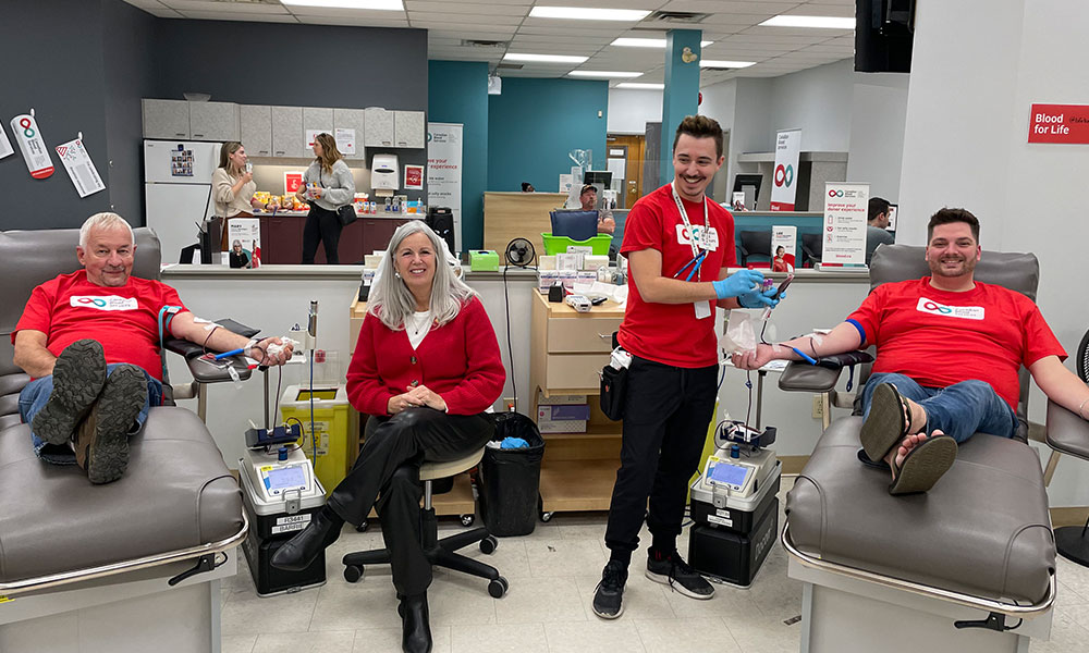 Two men donating blood, while another man assists and a woman sits in the middle.