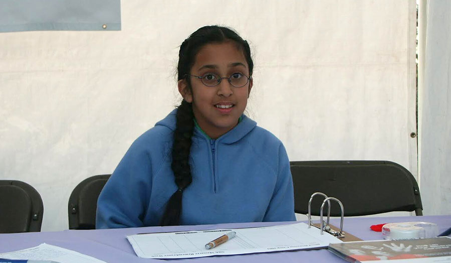 Sikh Nation volunteer, Jastej, seated at a table with a binder and pen on it. Jastej wears a blue sweater and glasses.