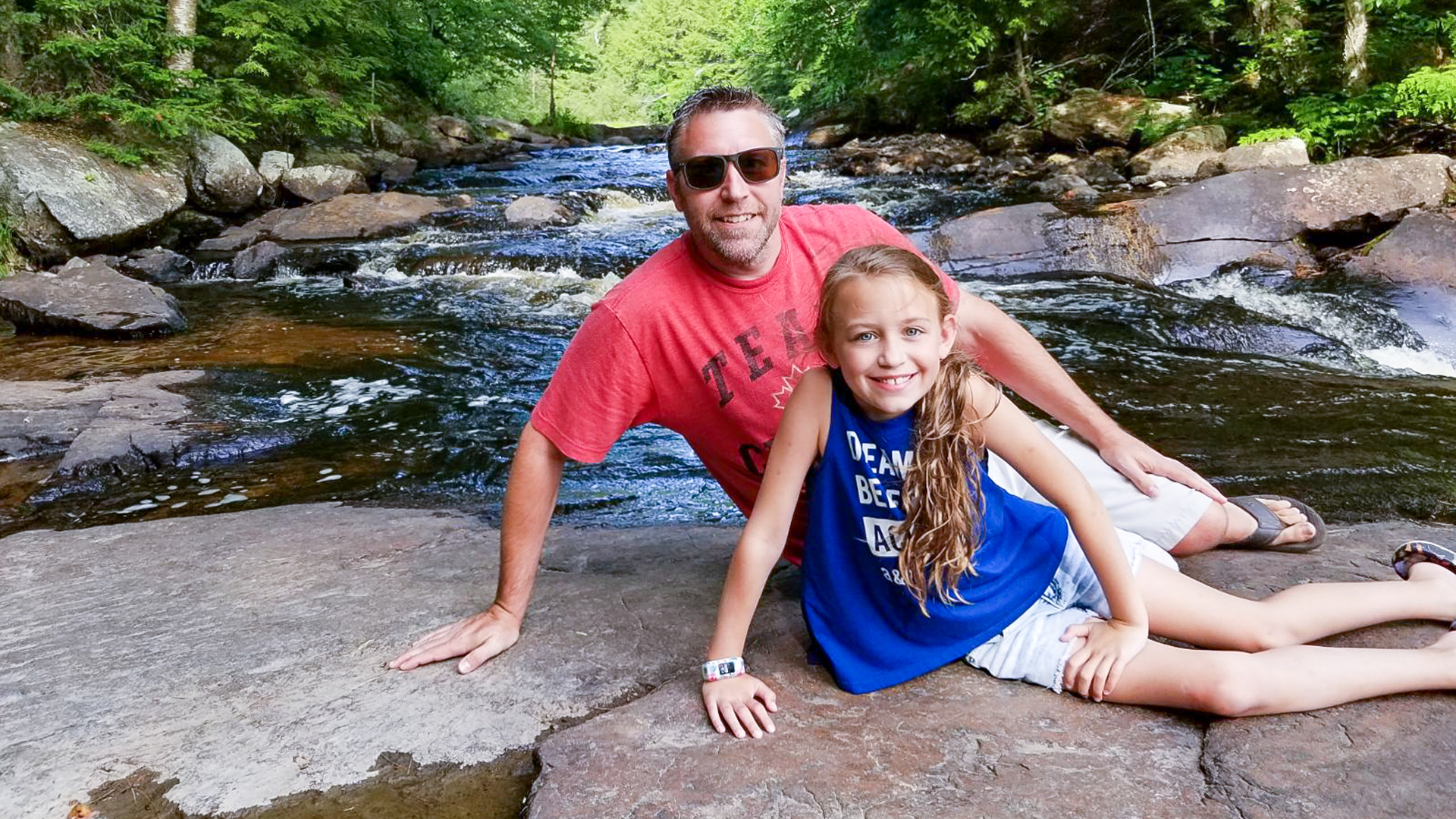 Jeff Brown with his daughter Preslee sit together on rocks in a stream in the woods. Jeff received immunoglobulin, a medication made from plasma, to treat Guillain-Barré syndrome (CBS).