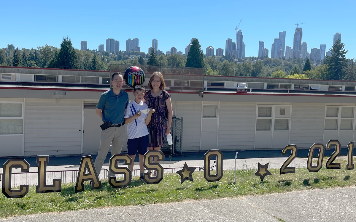 Celia and Marcus Lau pose with their son Justin behind a “class of 2021” yard sign on the day of his graduation.