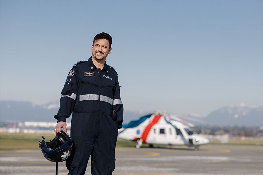 Critical care flight paramedic in uniform holding helmet with air ambulance in background