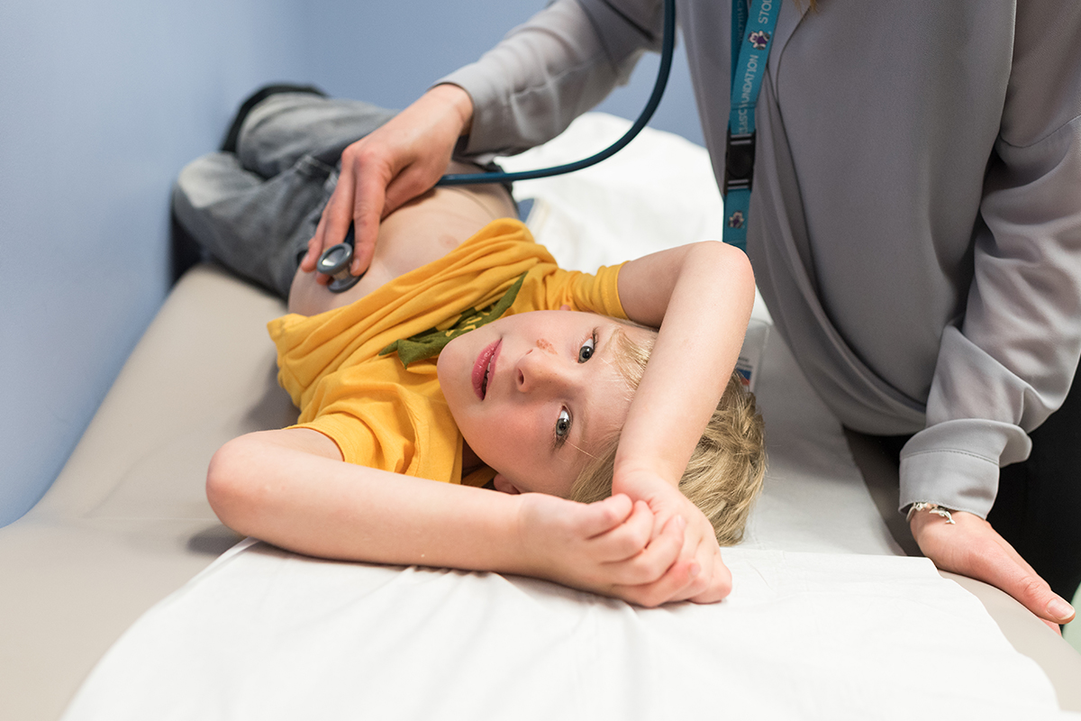 Boy in yellow shirt on hospital bed being checked with a stethoscope