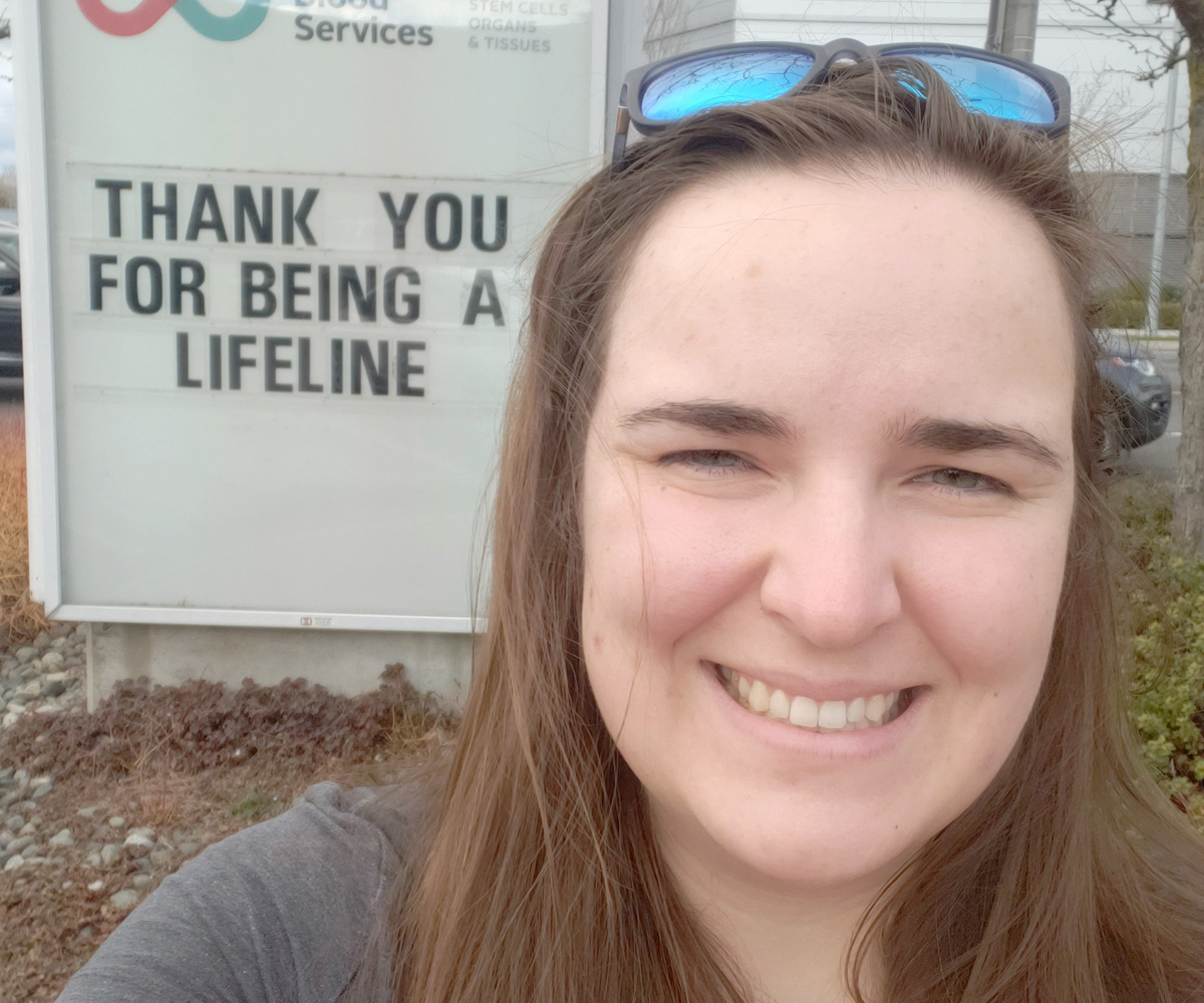 Woman takes a selfie in front of a Canadian Blood Services sign with a message of thanks to donors