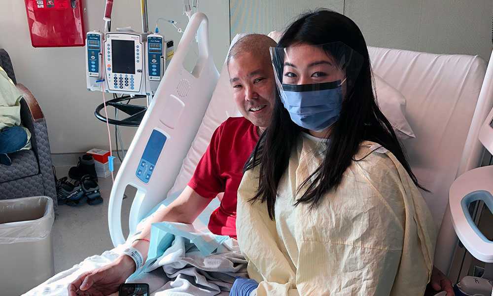 Woman wearing mask, face shield and gown in hospital with father receiving stem cell