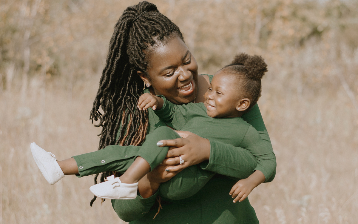 Adult woman holding her 2-year-old daughter in her arms with a field in the background