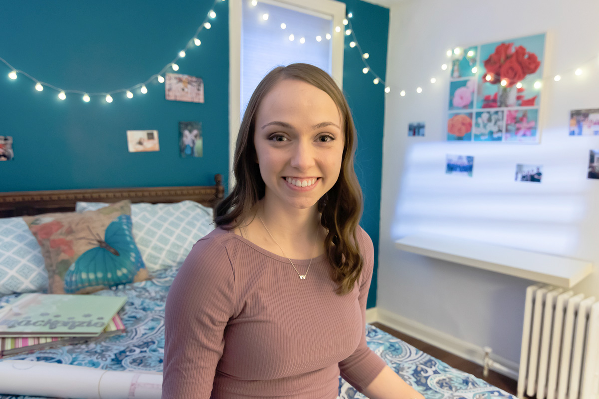 A young woman who is a childhood cancer survivor sitting on her bed.