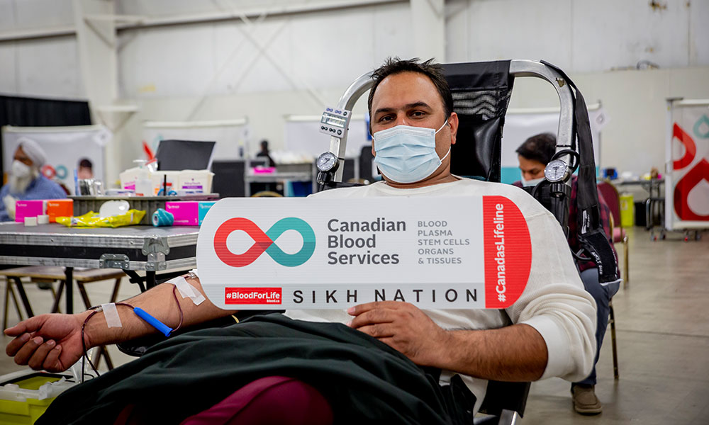 Man donating blood holding a Sikh Nation sign
