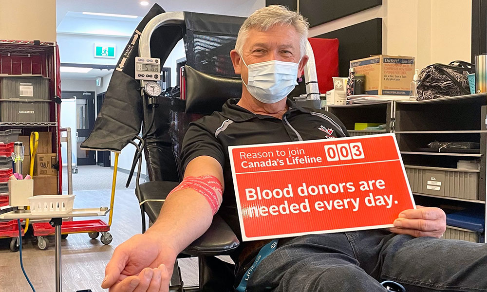 Blood donor in blood donation chair holding sign that says “Blood donors are needed every day”