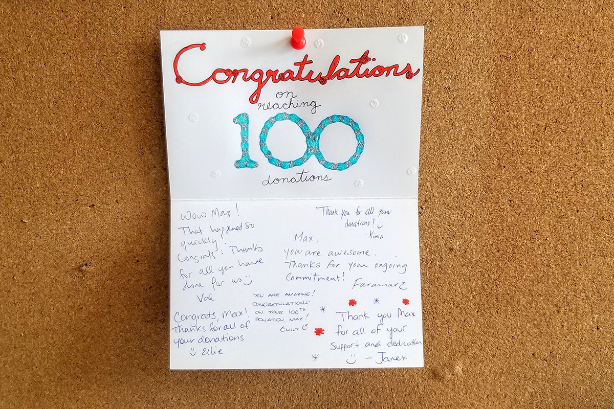 A signed, handwritten card on a bulletin board with the message “Congratulations on reaching 100 donations”