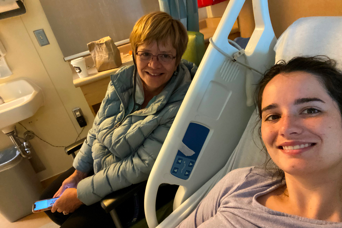 Young woman smiling, laying in hospital bed, with mother by her side