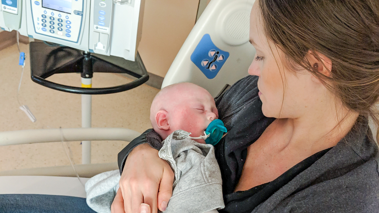 Image of Deanna Kitchen holding her son Cole Kitchen with an IV inside of him during his treatment for Diamond-Blackfan anemia in the hospital bed at SickKids