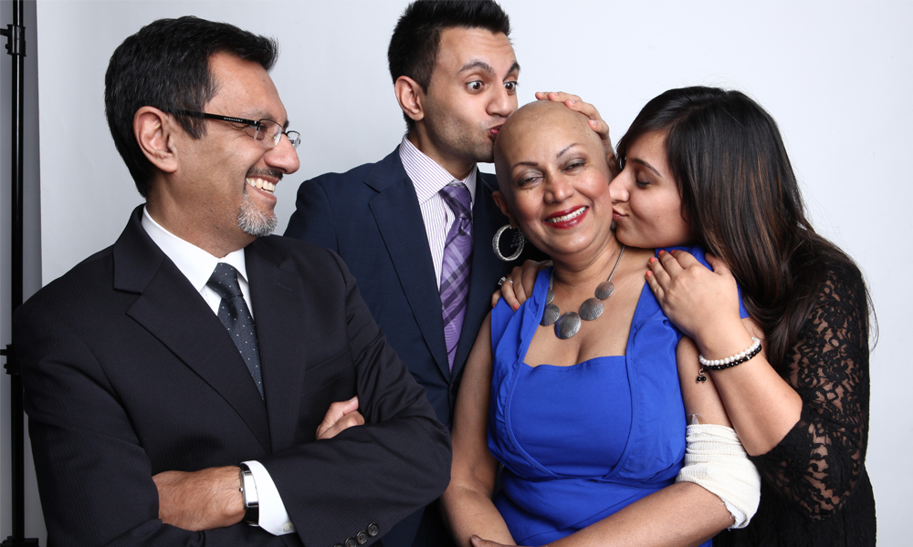 Munira Premji, who has had blood transfusion procedures during treatment for three different cancers, gets kisses from her grown son and daughter while her husband looks on, smiling.