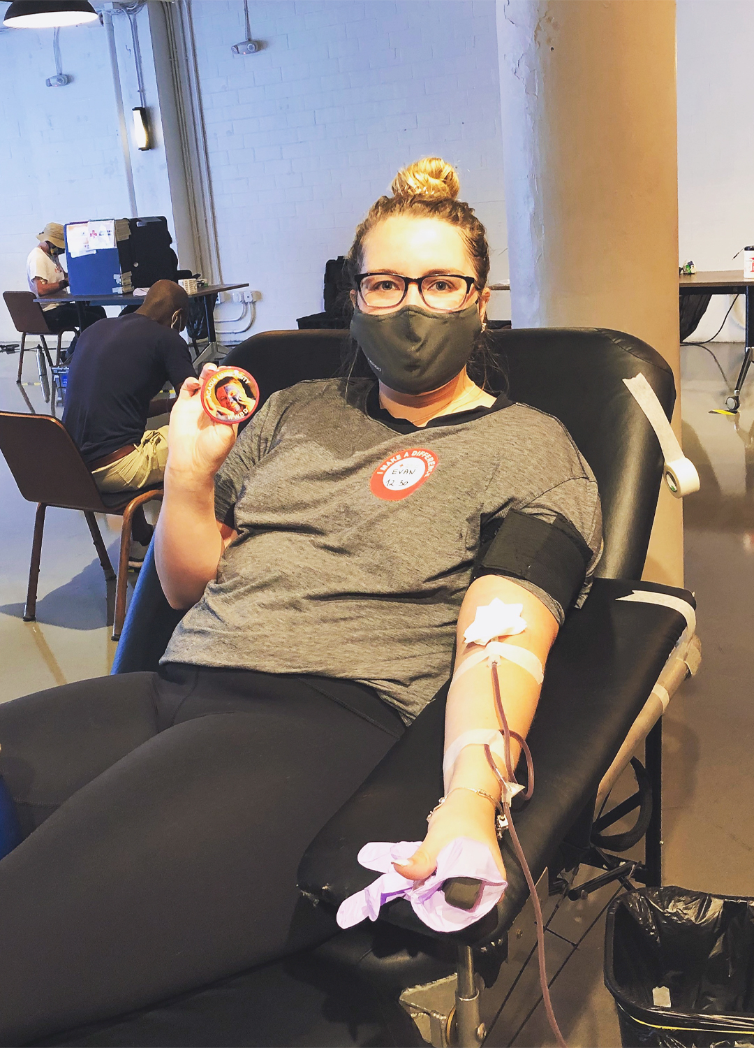 Image of Evan Phinney donating blood sitting in a chair holding up a button