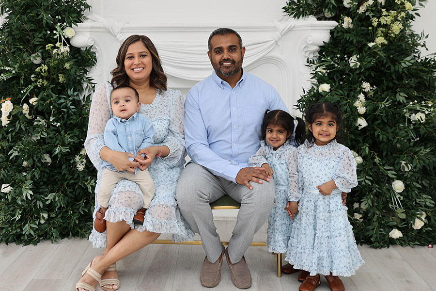 Une famille de cinq pose assise à l’intérieur, entourée d’arbres et de fleurs blanches